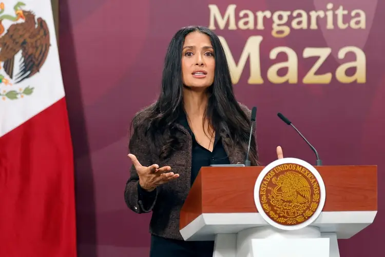 Woman in black jacket gesturing while speaking at a podium with official seal, with Mexican flag and purple banner behind her MEXICO-GOVERNMENT-CINEMA-INCENTIVE