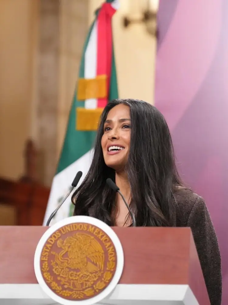 Woman speaking at a podium with an official seal, with a Mexican flag visible in the background Woman speaking at a podium with an official seal, with a Mexican flag visible in the background