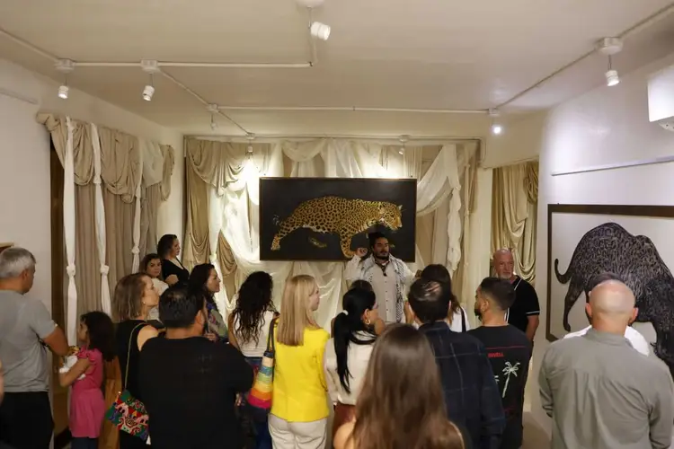 A group of people gather in an art gallery viewing paintings of leopards and other wildlife displayed on white walls _NF_1561