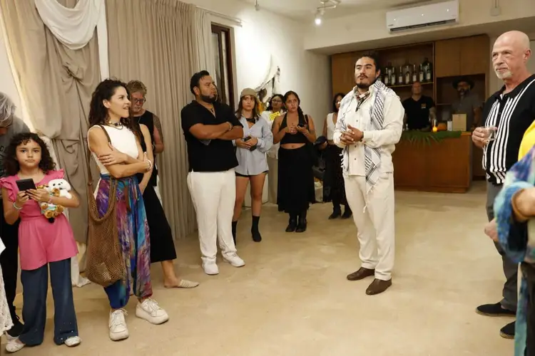 A group of people gather in an indoor venue, with a man in a cream-colored suit speaking to the crowd while others stand and listen around the room _NF_1695