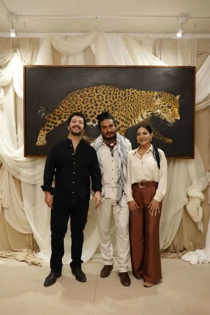 Three people stand together in front of a large framed painting of a leopard against a backdrop of cream-colored draped fabric _NF_1751