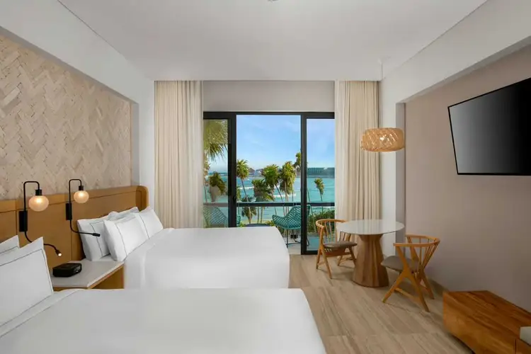 Hotel room with two beds, wooden headboards and pendant lamps, overlooking a tropical waterfront with palm trees through floor-to-ceiling windows Hilton-Tulum-Riviera-Maya-All-Inclusive-Resort