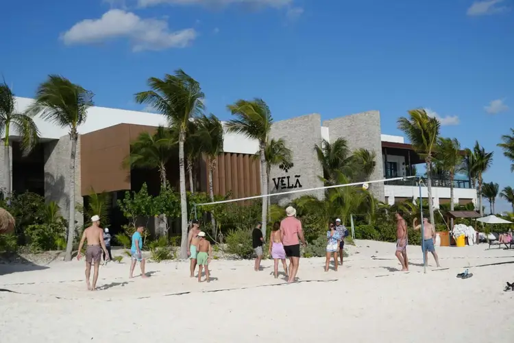 People play volleyball on a beach in front of a modern beachfront building with palm trees under blue sky People play volleyball on a beach in front of a modern beachfront building with palm trees under blue sky