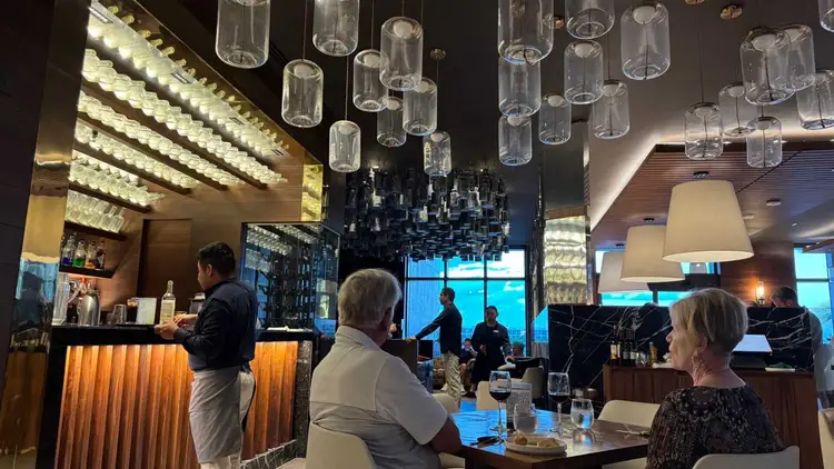 Interior of a modern hotel restaurant with diners seated at tables, a bartender at the counter, and hanging glass pendant lights overhead Interior of a modern hotel restaurant with diners seated at tables, a bartender at the counter, and hanging glass pendant lights overhead