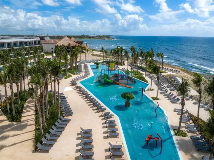 Beachfront resort with curved blue pool, water playground, palm trees, lounge chairs, and ocean views under blue sky photo-hilton-tulum-riviera-maya-all-inclusive-resort-tulum-9