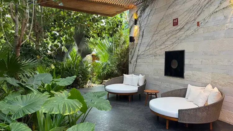 Lounge chairs with white cushions sit on a patio surrounded by tropical plants and a white stone wall Lounge chairs with white cushions sit on a patio surrounded by tropical plants and a white stone wall