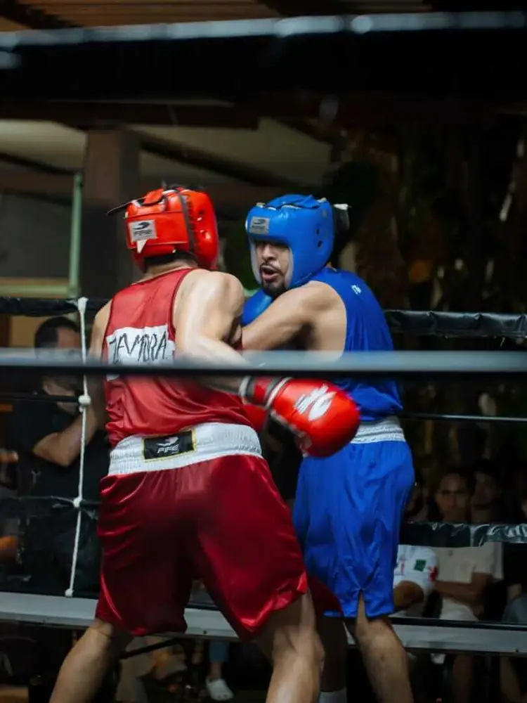 Two amateur boxers in red and blue uniforms and protective headgear exchange punches in a boxing ring during a match