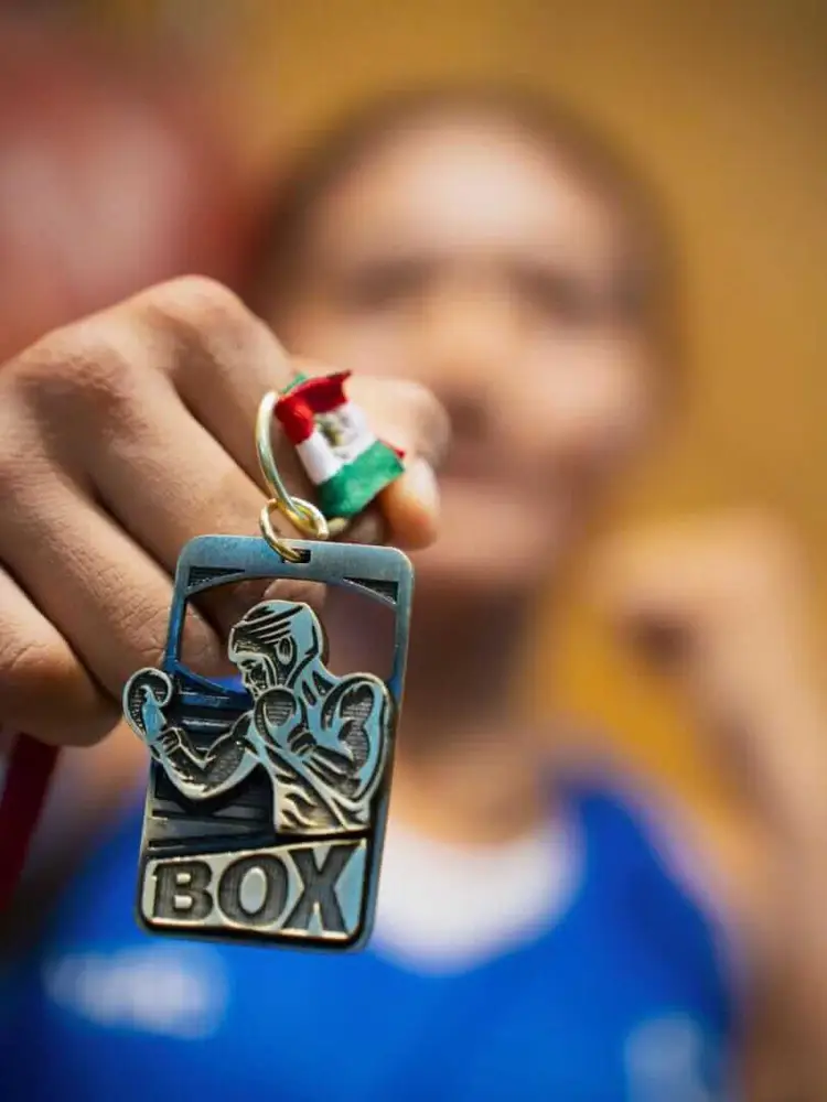 Person's hand displays a boxing medal with tricolor ribbon and a ring with flag colors