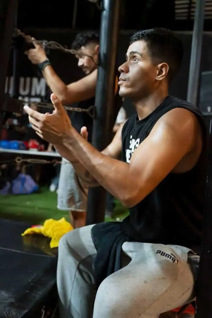 Man in black sleeveless shirt watches boxing training activity in an indoor gym facility