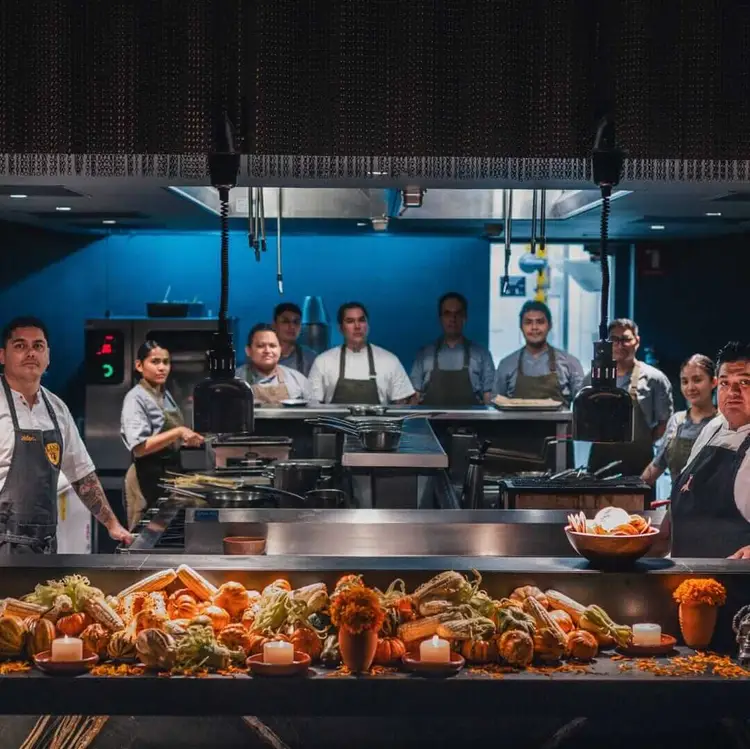 Restaurant kitchen staff stand behind a counter displaying seafood and produce, with the open kitchen visible behind them under blue lighting 465700998_18004093358659103_6384853058021368322_n