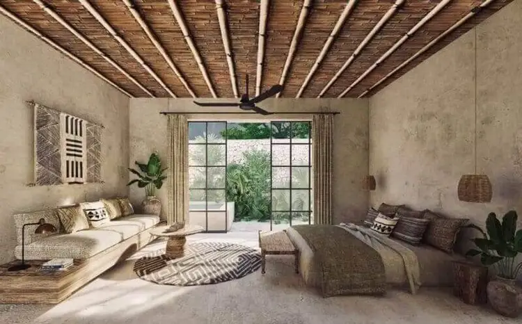Spacious bedroom with exposed wooden ceiling beams, concrete walls, a bed with patterned bedding, seating area, potted plants, and large glass doors opening to