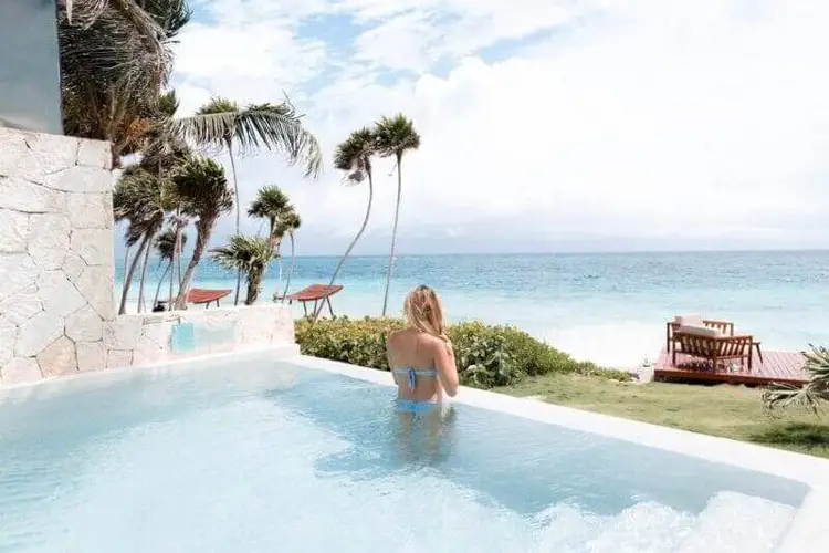 Woman in a beachfront pool overlooking the ocean with palm trees and sandy beach visible beyond