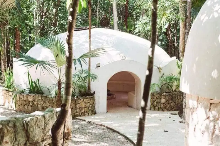 White domed structure with arched entrance surrounded by tropical vegetation and stone walls in a forested setting