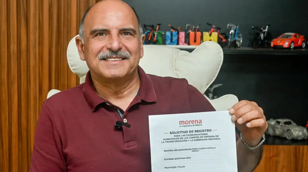 Jorge Portilla registers with Morena for Tulum’s 2027 municipal race Man in maroon polo shirt holds up a Morena party registration document while seated in an office with toy cars displayed on shelves behind him