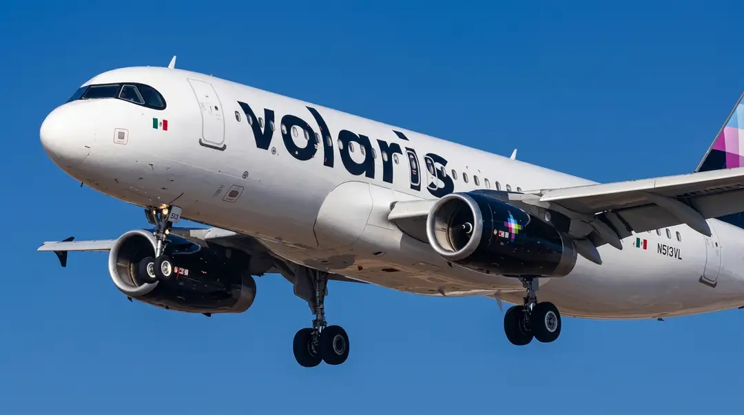 Commercial aircraft in flight with landing gear down against a clear blue sky