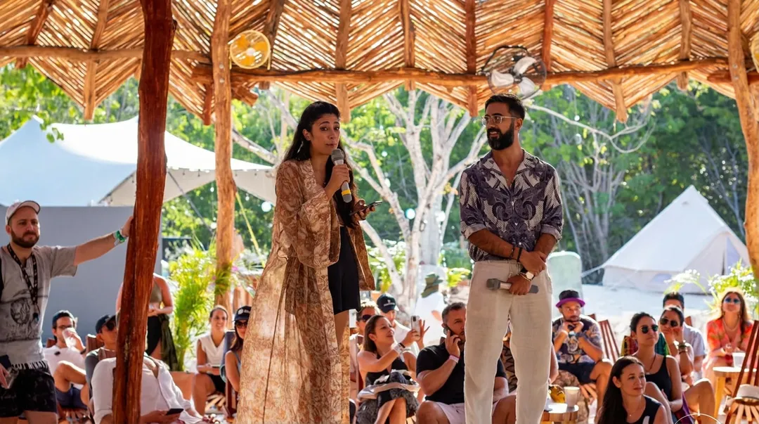 Tulum Innovation Fest runs December 9 to 12 at IKAL Arena Two speakers present on stage under a wooden structure while an audience sits watching during an outdoor event