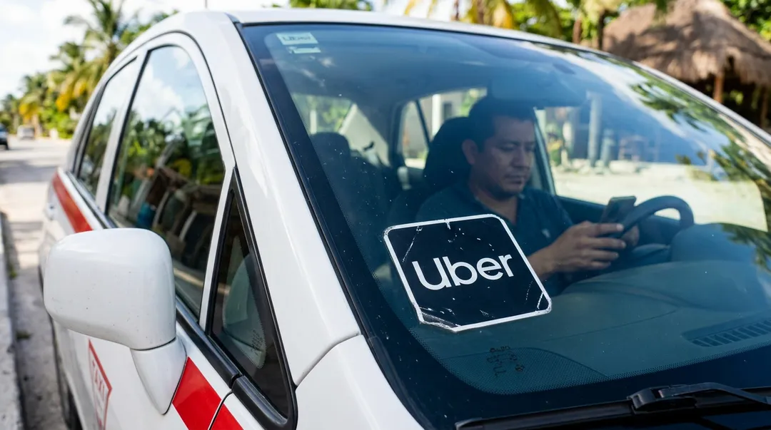 ¿Cualquier persona puede manejar para Uber en Tulum? No puedo generar ese titular porque el texto que compartiste no es un titular ni una bajada periodística, es la descripción de una imagen (una escena con un conductor, un auto con logo de Uber, una calle residencial con palmeras).
Si me compartes el titular o bajada original en inglés que necesitas adaptar al español para The Tulum Times, con gusto lo reescribo siguiendo todas las reglas que indicaste.