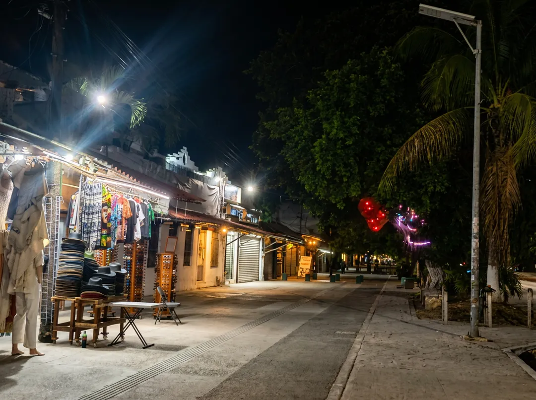 Night street scene with illuminated shops and palm trees lining a pedestrian walkway in a tropical location