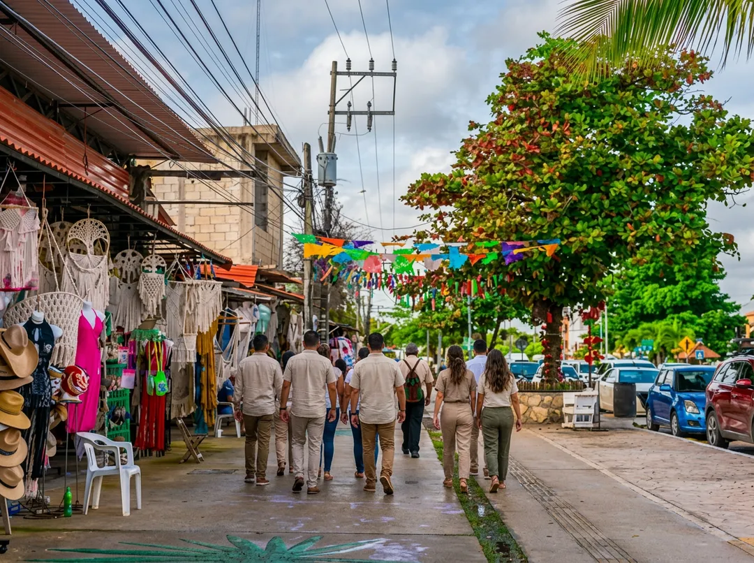 Nearly 300 Residents Launch Tulum Unido Movement to Demand Government Transparency and Accountability People walk through a street market lined with vendor stalls and colorful decorations under a large tree