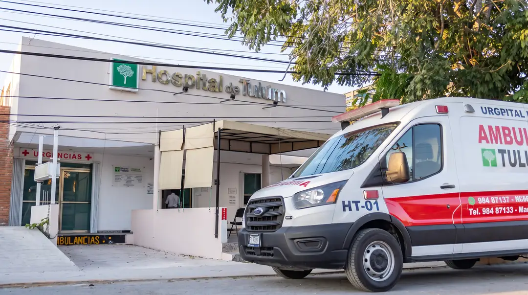 An ambulance parked outside the entrance of a hospital building with a green and gray sign