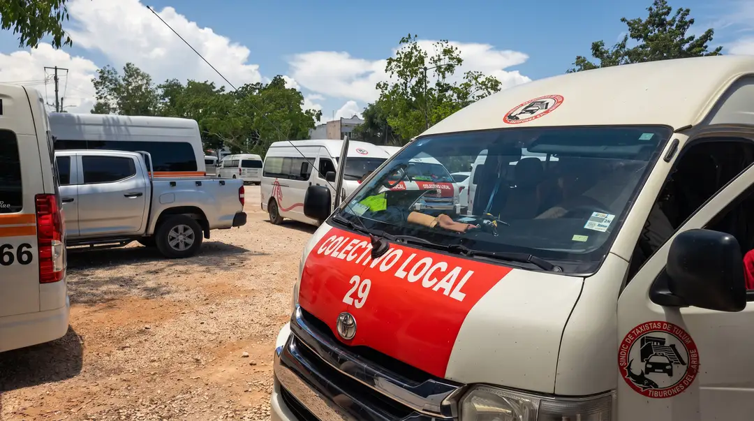 Several minibuses and vans are parked in a dirt lot under clear skies, with a red and white vehicle marked "29" prominently displayed in the foreground