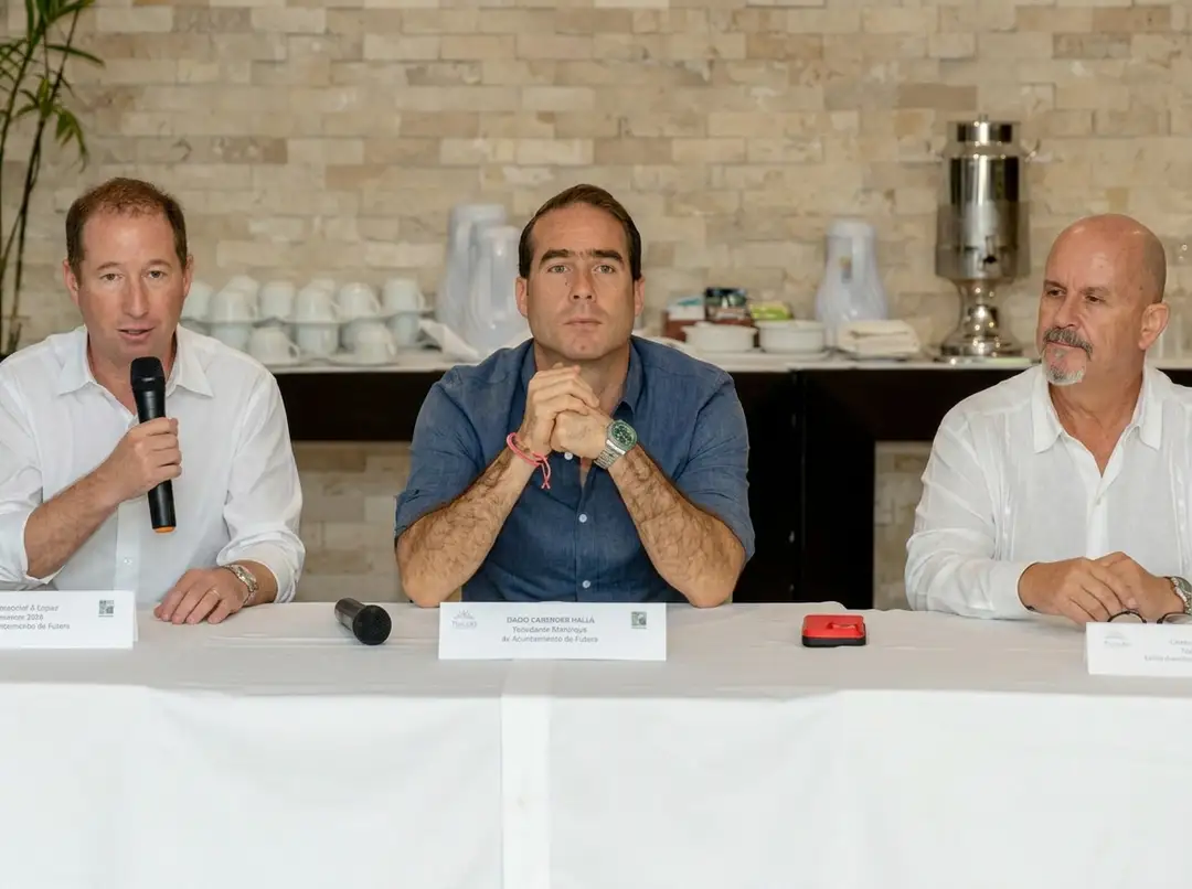Three men sit at a table during a panel discussion in front of a brick wall and kitchen counter