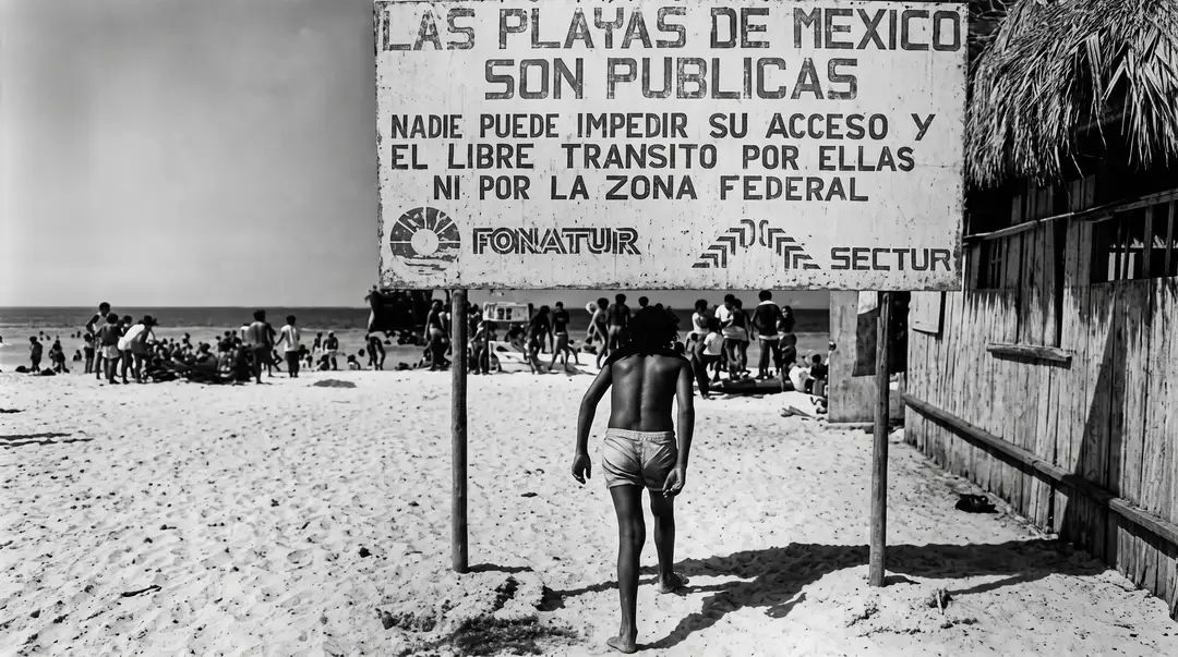 A shirtless man walks toward a large weathered sign on a sandy beach with other beachgoers and structures visible in the background