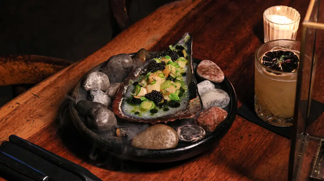 Eight Michelin plaques came to Tulum on Friday Plated oyster dish with garnishes served on a dark slate plate next to a glass of beverage on a wooden table