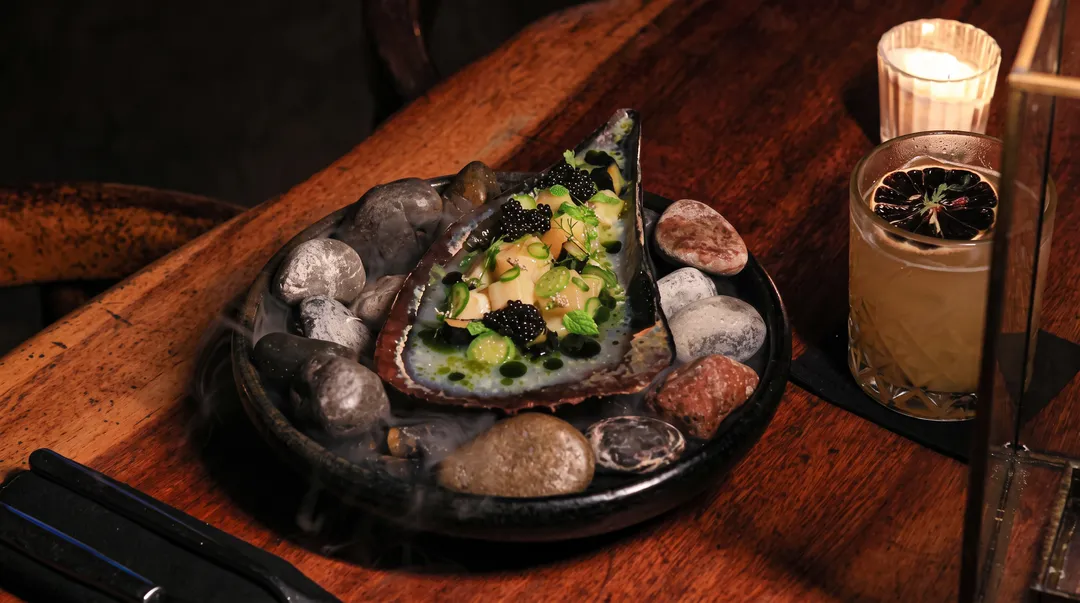 Eight Michelin plaques came to Tulum on Friday Plated oyster dish with garnishes served on a dark slate plate next to a glass of beverage on a wooden table