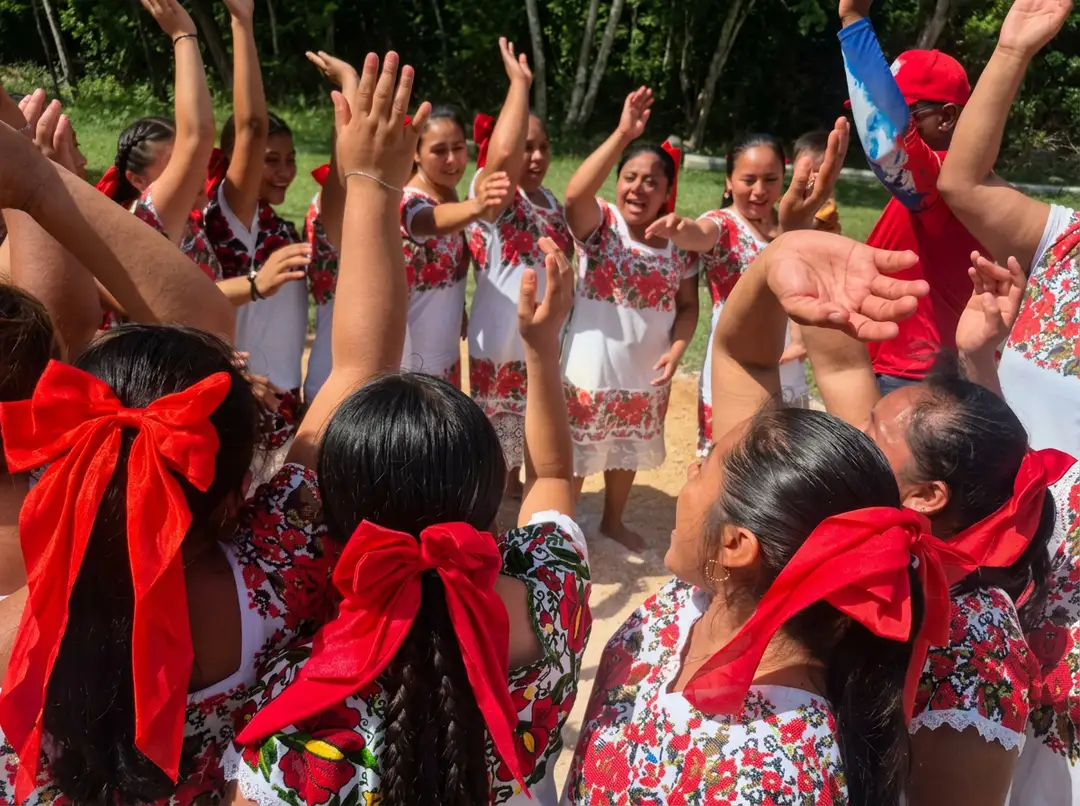 Group of children wearing matching floral dresses and red bows celebrate together outdoors in a wooded area