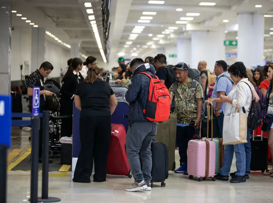 Travelers with luggage wait in line at an airport check-in counter