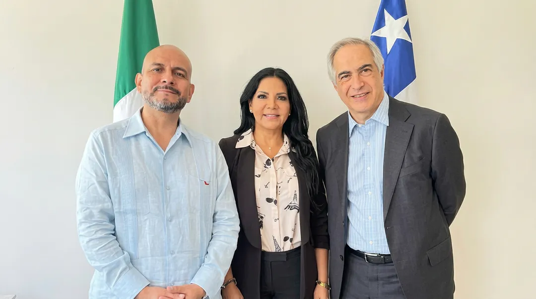Tres personas posan juntas para una fotografía formal frente a una bandera verde y una bandera azul con una estrella blanca