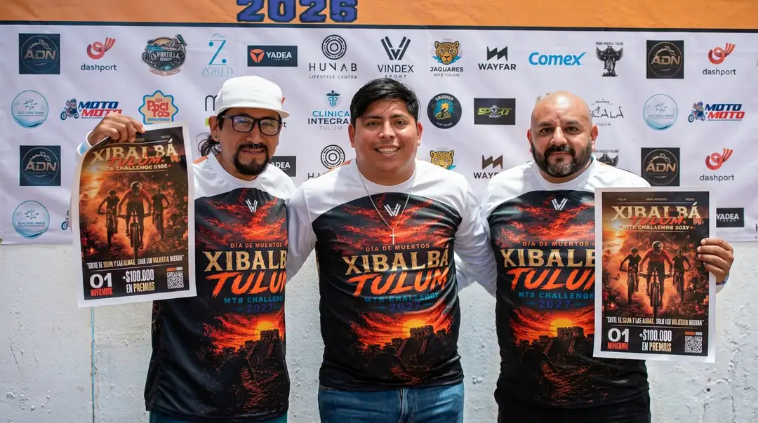 Three men hold promotional posters and wear branded shirts for a mountain bike race event in front of a sponsor backdrop