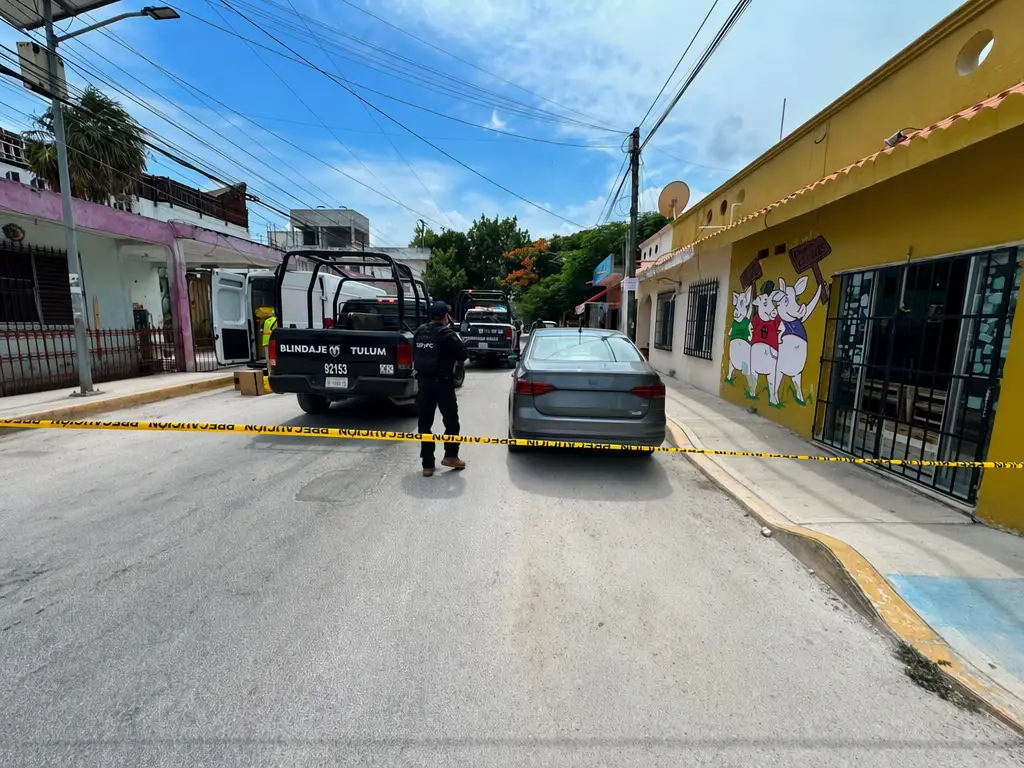 Police officers secure a street scene with yellow caution tape strung across the road between parked vehicles and storefronts