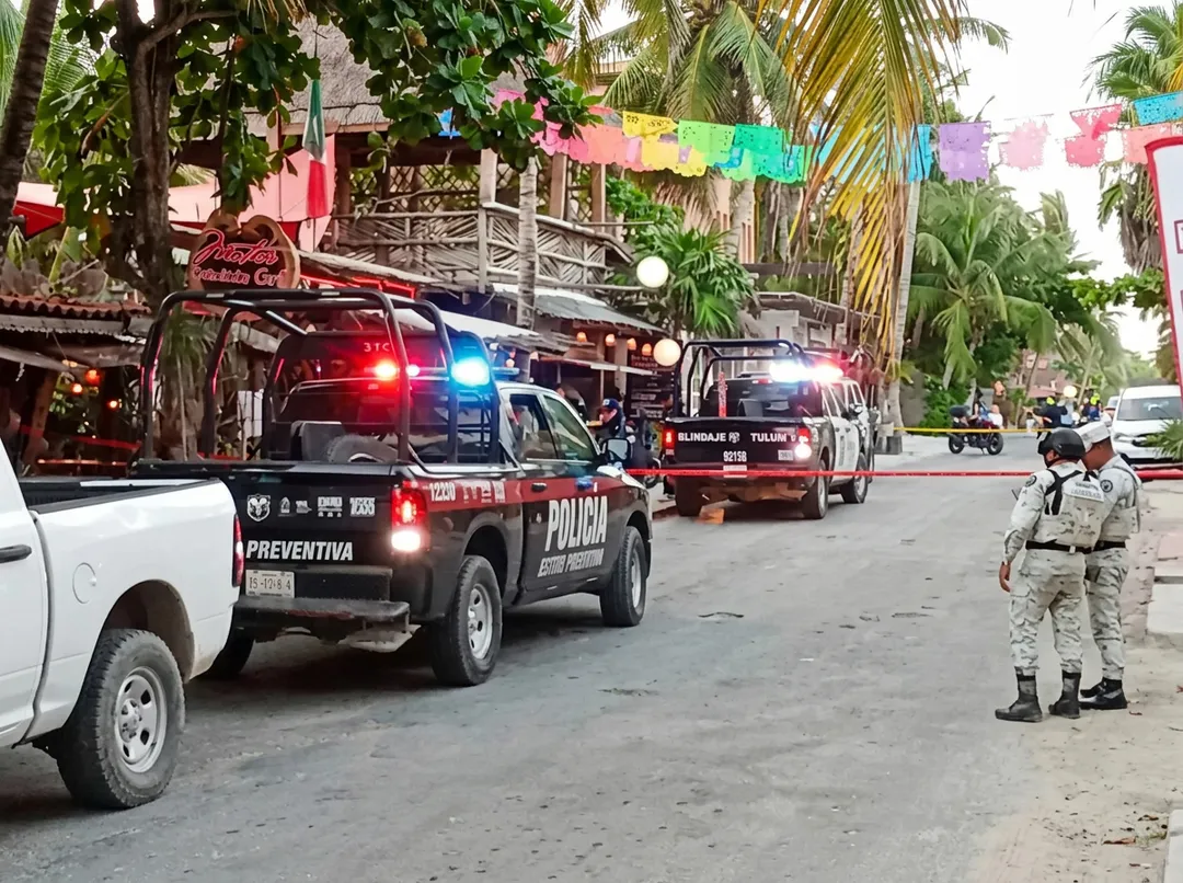 Federal Lawmakers Demand Sheinbaum Intervene as Tulum Tourism Crisis Deepens With Extortion Claims Police and emergency vehicles line a palm-tree-lined street in a tropical town, with an officer standing guard nearby