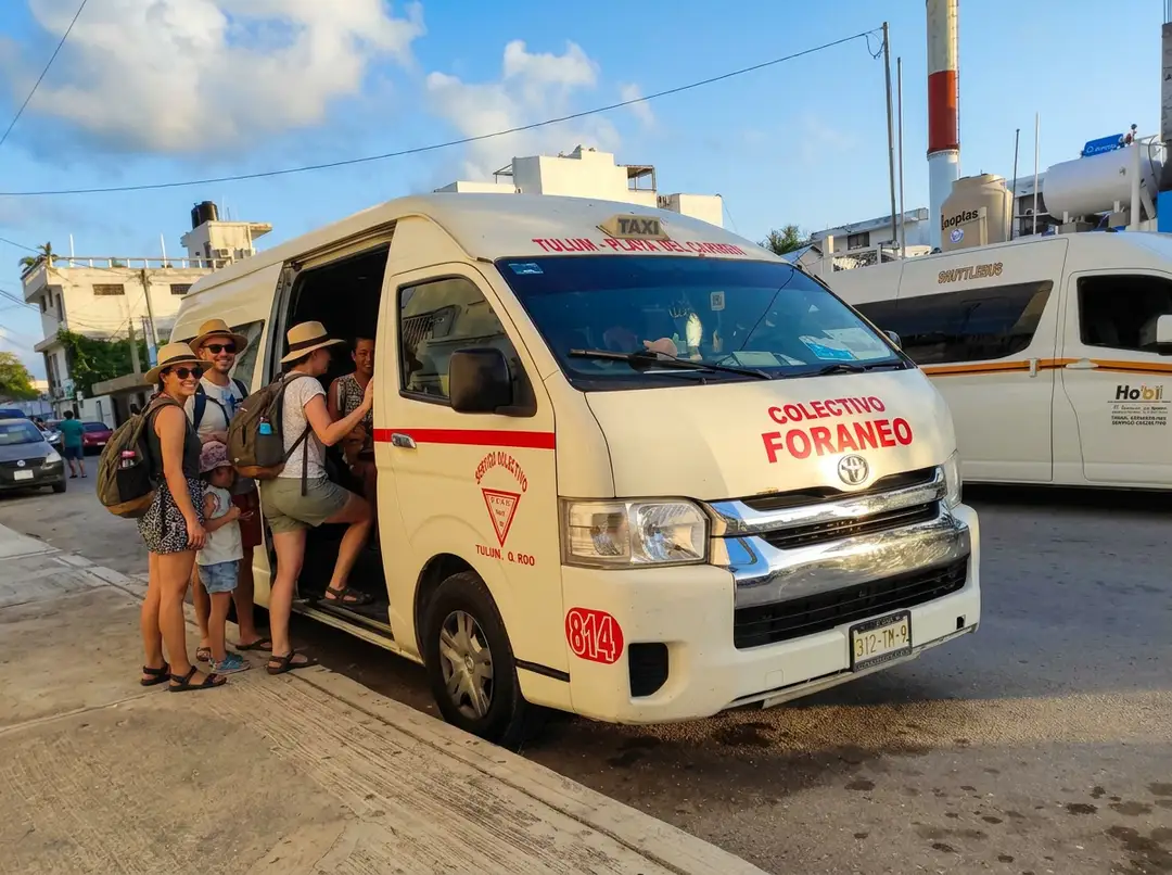 Roadside stops disappear in Tulum as every intercity pickup shifts to the bus terminals Passengers board a white minivan labeled "Colectivo Foraneo" at a street pickup point in an urban area