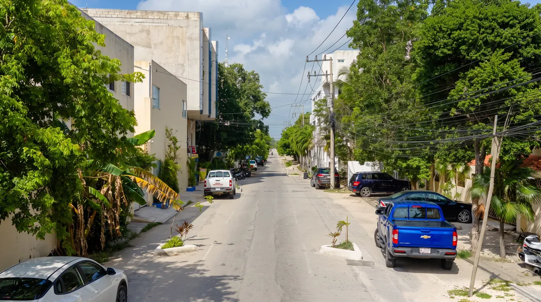 Why Is Calle 7 Always Under Construction in La Veleta? A quiet residential street lined with parked cars, concrete buildings, and green vegetation under a partly cloudy sky