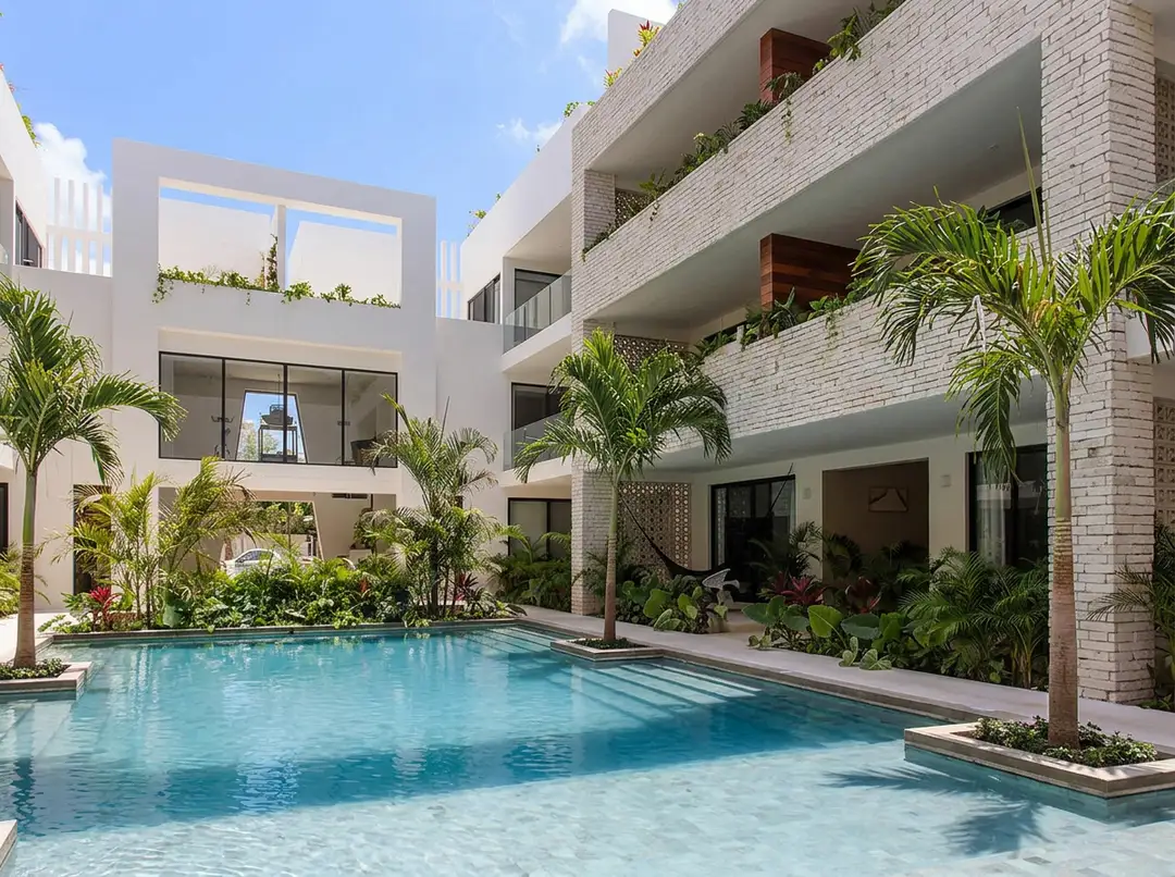 Tulum's property market is doing the zoning the boom skipped Modern multi-story residential buildings with balconies surround a swimming pool surrounded by tropical plants and palm trees