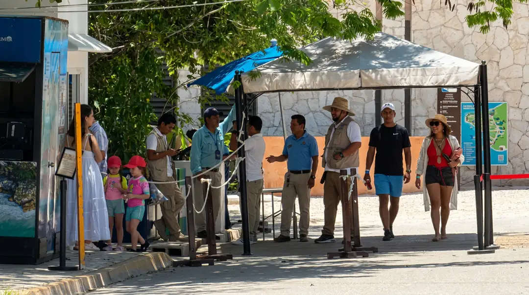 Tulum keeps paying for what happens before the ticket window A group of tourists and staff members gather under a shaded structure at what appears to be a ticketing or entrance area near a stone building