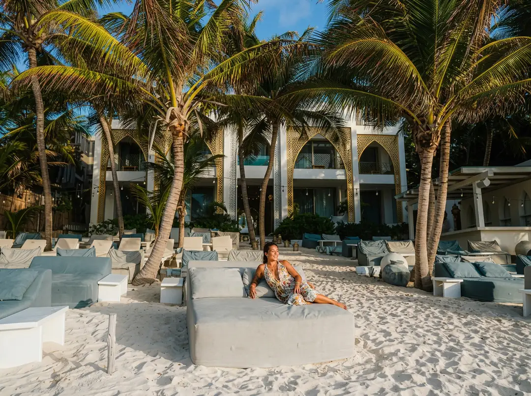 Riviera Maya hotels welcome federal push to revive Tulum tourism Person sitting on a concrete bed on a sandy beach in front of a white building with palm trees and lounge chairs