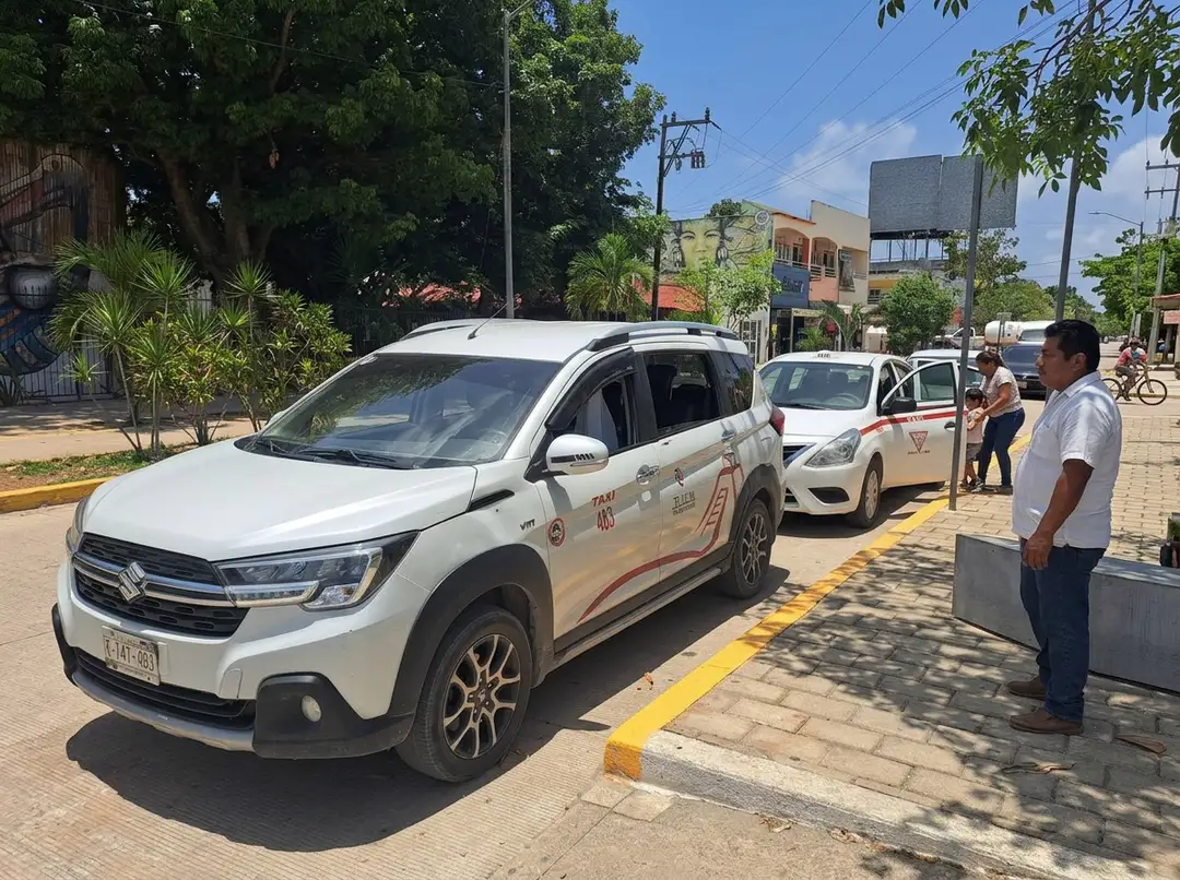 White taxis parked at a designated taxi stand on a paved street with few passengers and drivers waiting nearby
