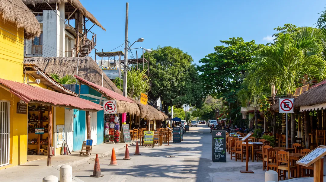 Beachfront shops and restaurants with thatched roofs line a pedestrian street under clear sky