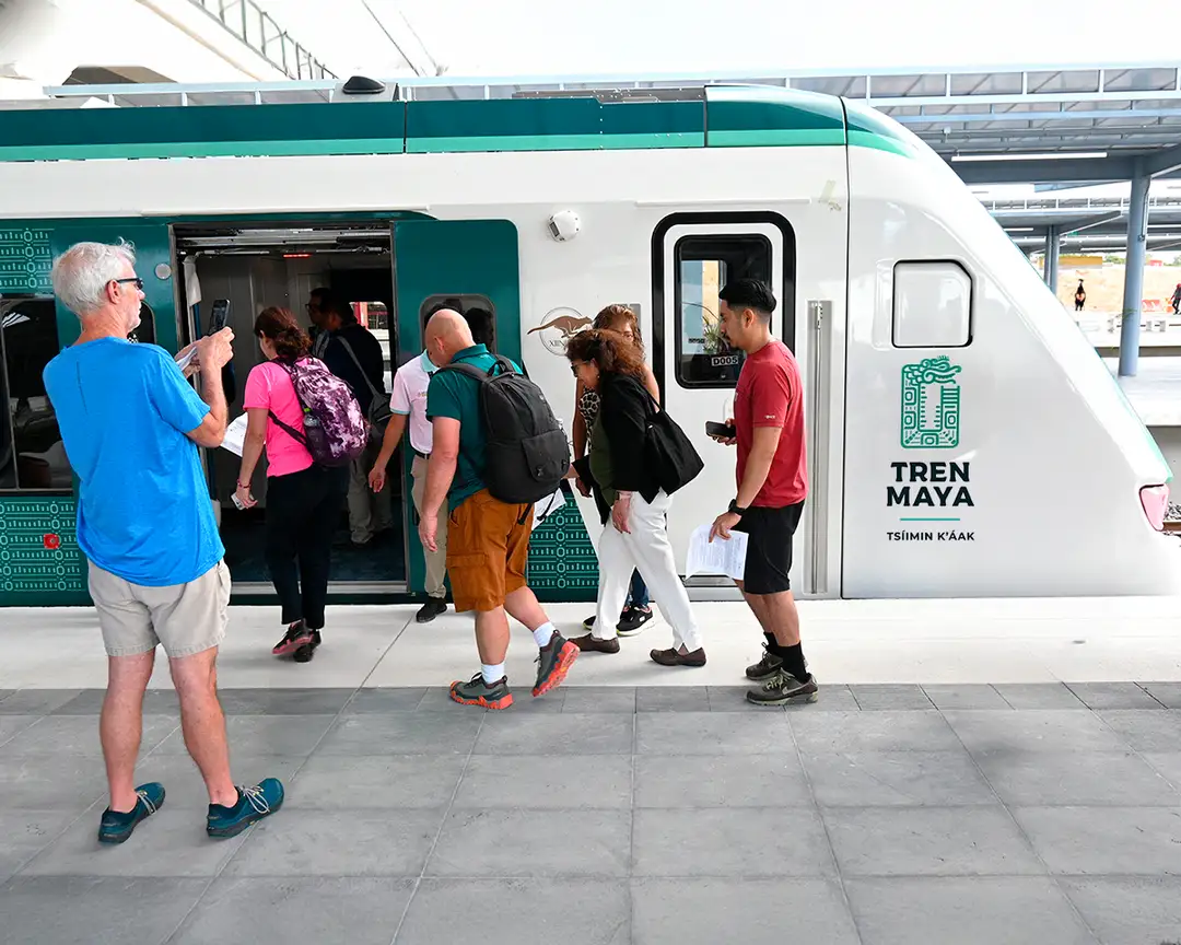 Passengers board a Tren Maya commuter train at a station platform