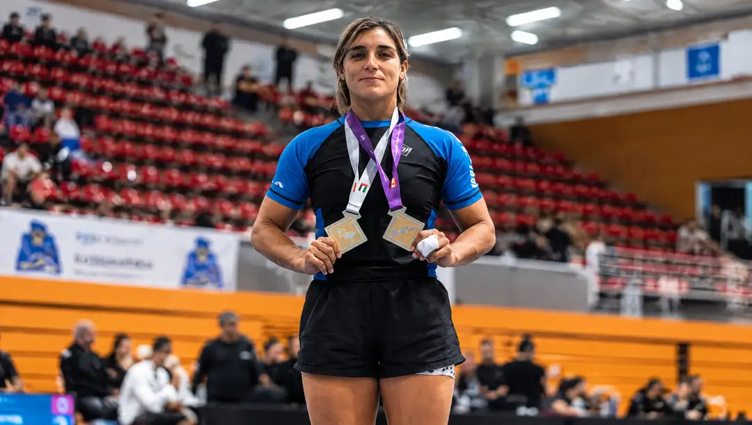 Tulum blue belt Amira Neme targets the IBJJF No-Gi Worlds Athlete wearing blue and black competition attire stands in an indoor arena holding two medals around her neck