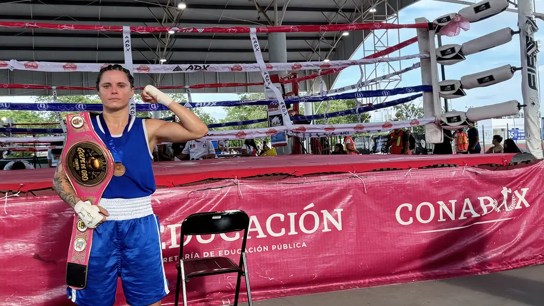 Boxer in blue uniform stands inside a boxing ring holding a championship belt