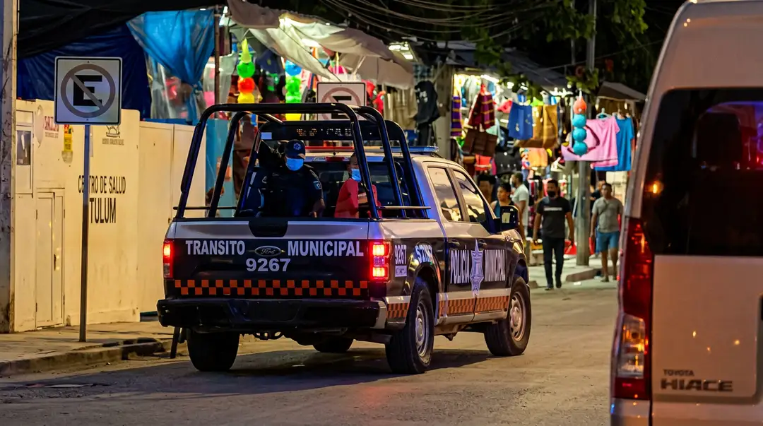 A municipal police vehicle patrols a busy street lined with shops and pedestrians at night