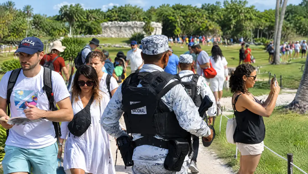 Who should sell Tulum, the army or the travel industry? A bilingual welcome sign for Parque del Jaguar stands at the entrance to a paved road lined with palm trees and tropical vegetation under clear blue sky