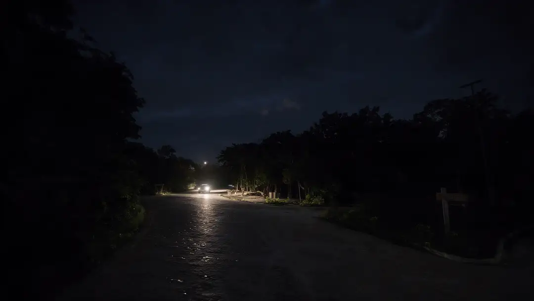 Why Tulum’s streets are going dark A dimly lit street lined with trees shows sparse streetlights illuminating a mostly dark roadway at night