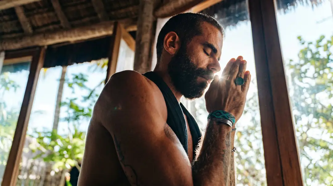 Yoga Teacher and Breathwork Facilitator in 21 Days, at a Jungle Retreat Near Tulum Man with beard and tattoos practicing breathwork or meditation indoors near open windows with tropical vegetation visible outside